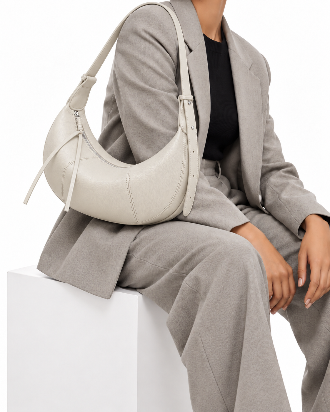 The Flavia Crescent Bag in Ivory, worn by a seated model in a grey suit