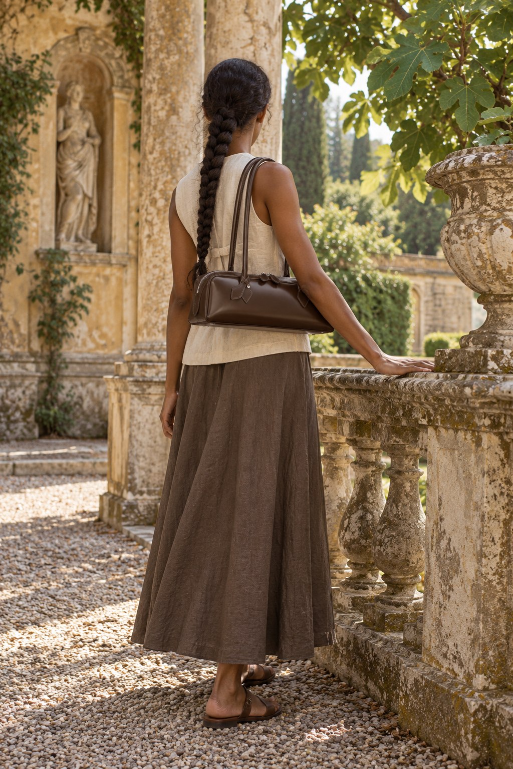 The Aurelia Bag in Espresso, worn on the shoulder beside a stone balustrade in a villa garden