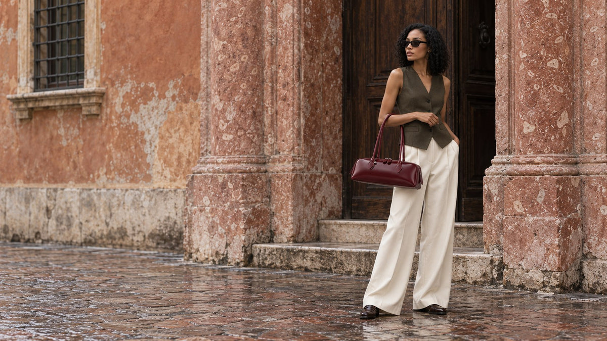 The Aurelia Bag in Barolo, carried by hand outside a rose marble palazzo doorway